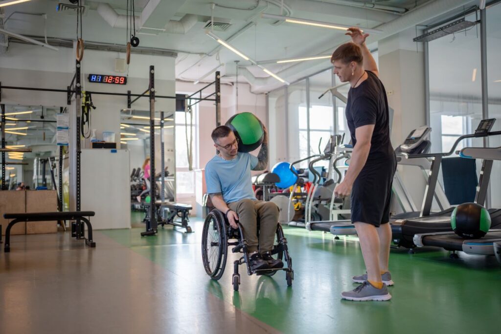 A man in a wheelchair does rehabilitation with a trainer.
