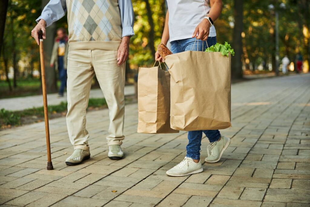 A support worker helps an elderly man with his groceries.